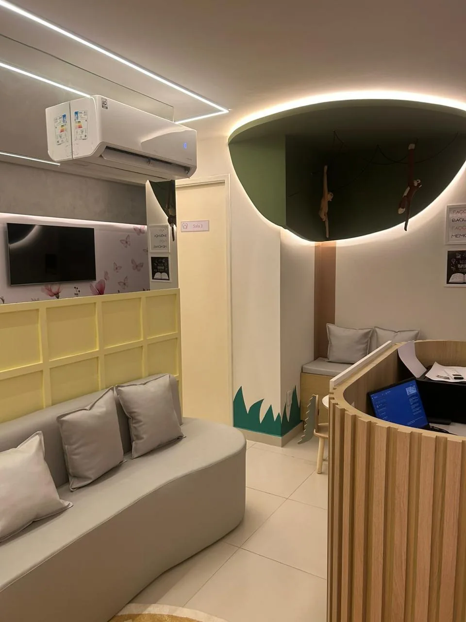 Recepção da Afeto Há em Fortaleza, com sofá cinza curvo, painel amarelo e teto em forma de copa de árvore com macaquinhos