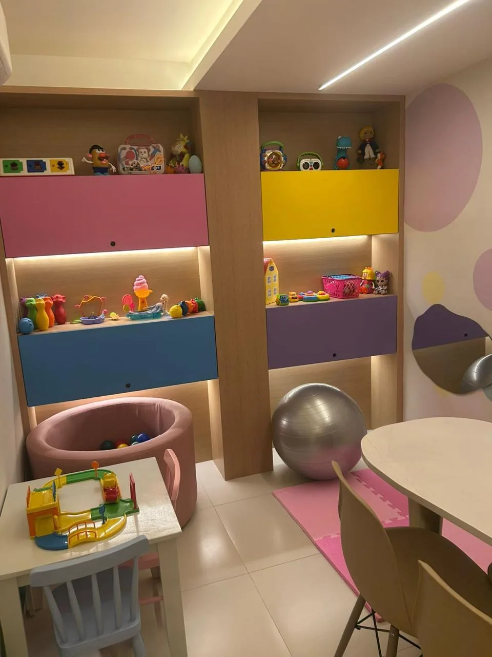 Sala de terapia infantil com armários coloridos, piscina de bolinhas, bola suíça, tapete de EVA e mesa infantil